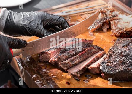 Gloved hands of a chef slicing a portion of delicious juicy tender roast beef brisket with a large knife in a close up on the blade and cutting board Stock Photo