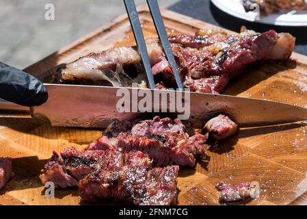 Chef cutting freshly grilled meat off the BBQ with a large knife on a wooden cutting board in a close up view on the food Stock Photo