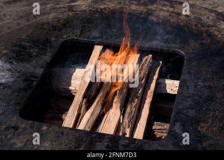 Logs on a barbecue fire beginning to burn in a high angle view inside a metal griddle in a healthy lifestyle and renewable fuel concept Stock Photo