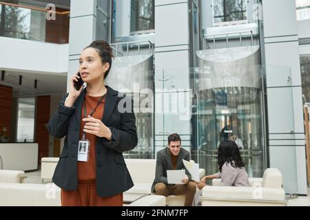 Young businesswoman talking on mobile phone while her colleagues working in the background at office Stock Photo