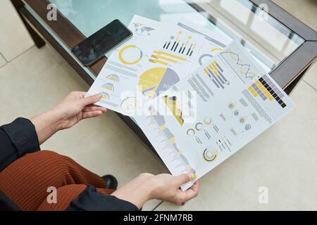 Close-up of businesswoman sitting at the table and examining financial report with graphs Stock Photo