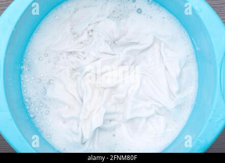 White cloth, shirt, t-shirt soaking in plastic blue basin with foamy water, close-up Stock Photo