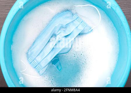 Disposable medical mask soaking in blue plastic basin with water with foam for second use, concept picture about virus and protection Stock Photo