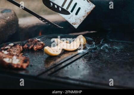 Wonderfully fragrant and crispy pork neck is prepared on a granite stone on an open fire. Next, a man prepares a baked apple as a dessert for the main Stock Photo