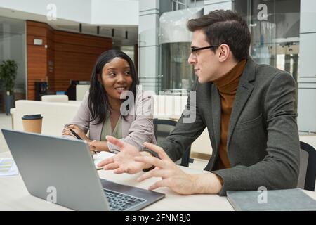 Business colleagues sitting at the table and discussing online work together using laptop Stock Photo