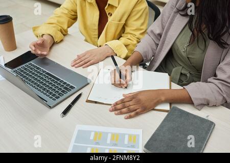 Close-up of two colleagues working in team at the table they working on laptop and making notes in notebook Stock Photo