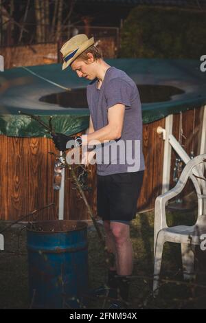 Hardworking man in work clothes uses loppers to split wood into smaller sticks to fit into the kiln for burning. Work in the garden. Grooming the plot Stock Photo