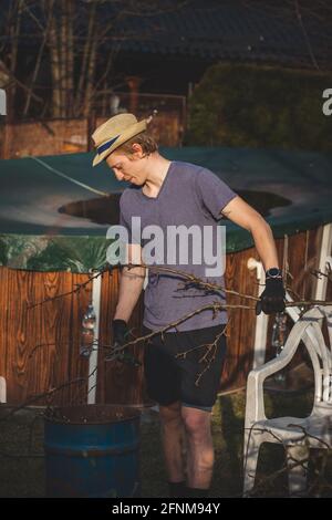 Hardworking man in work clothes uses loppers to split wood into smaller sticks to fit into the kiln for burning. Work in the garden. Grooming the plot Stock Photo