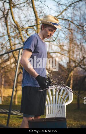 Hardworking man in work clothes uses loppers to split wood into smaller sticks to fit into the kiln for burning. Work in the garden. Grooming the plot Stock Photo