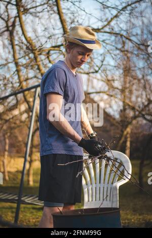 Hardworking man in work clothes uses loppers to split wood into smaller sticks to fit into the kiln for burning. Work in the garden. Grooming the plot Stock Photo