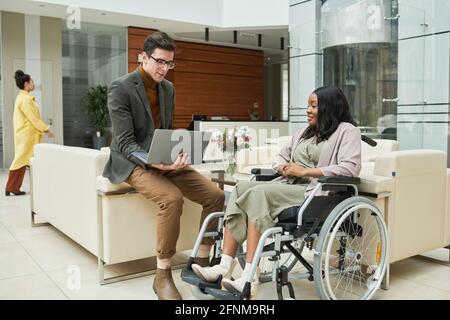 Businessman working on laptop and talking to disabled businesswoman they working in team at office Stock Photo