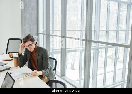 Young businessman sitting at the desk and examining business documents at office Stock Photo