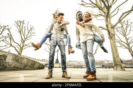 Happy multiracial friends couples having fun with piggiback in winter time waiting spring - Friendship concept with multicultural young people Stock Photo