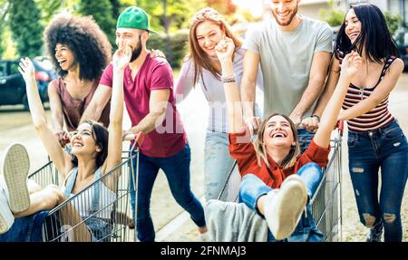 Young multiracial people having fun together with shopping cart - Millenial friends sharing time with trolleys at commercial mall parking Stock Photo