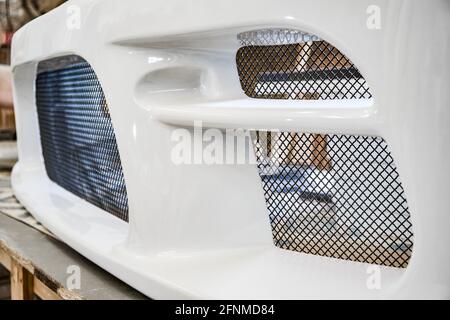 Thin metal grid installed on white shiny bumper of contemporary automobile in car tuning station extreme close view Stock Photo