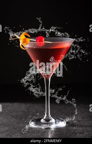 Traditional Manhattan cocktail with cherry splashing in glass on black background Stock Photo