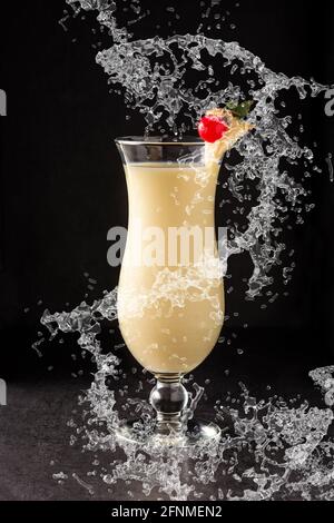 Pina colada cocktail splashing in glass on black background Stock Photo