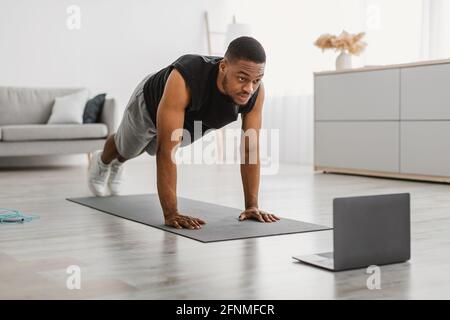Sporty Black Guy Exercising At Laptop Doing Plank At Home Stock Photo