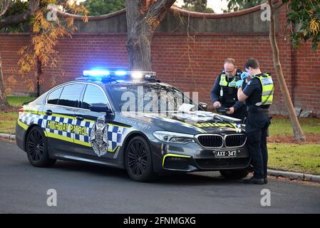 A Victoria Police Highway Patrol BMW M5, with lights flashing, parked on the side of the road, while two police officers perform their duty Stock Photo