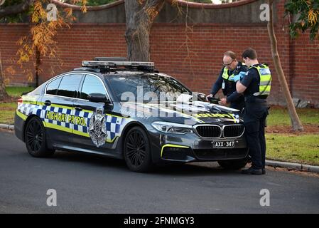 A Victoria Police Highway Patrol BMW M5 parked on the side of the road, while two police officers perform their duty Stock Photo