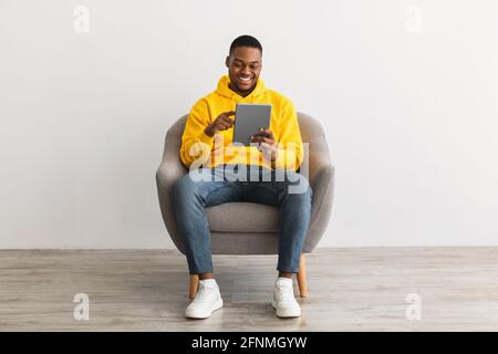 Happy Black Guy Using Digital Tablet Browsing Internet, Gray Background Stock Photo