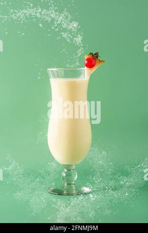 Pina colada cocktail splashing in glass on green background Stock Photo