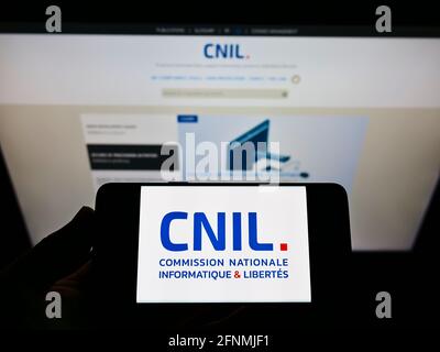 Person holding mobile phone with logo of French data protection authority CNIL on screen in front of webpage. Focus on cellphone display. Stock Photo