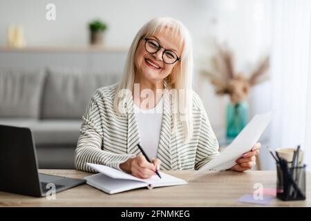 Smiling mature woman writing and holding document at home Stock Photo