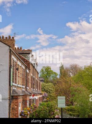 A row of terraced houses one of which is a guest house. Colourful hanging baskets are on display and a blue sky with clouds is above. Stock Photo