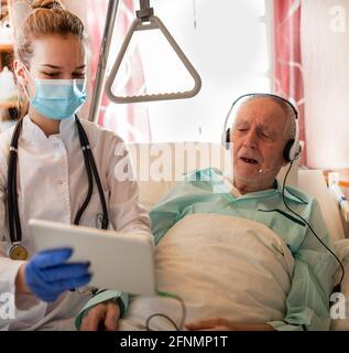 Senior man in hospital having conference call on tablet with his family. Nurse helping him with technology Stock Photo