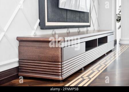 Elegant new cabinet for TV set made of veneer and solid oak lumber toned in dark brown color near molded wall in light room Stock Photo