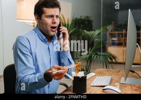Confused handsome young business man using mobile phone while having lunch at the work Stock Photo