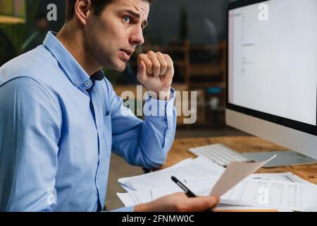 Young pensive business man working with papers while sitting in the office. Successful entrepreneur is studying documents with attentive and concentra Stock Photo