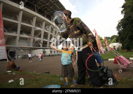 A soap bubble itinerant helping a child on playing soap bubbles outside Main Stadium in Senayan Sports Complex (Gelora Bung Karno) in Jakarta, Indonesia. Stock Photo