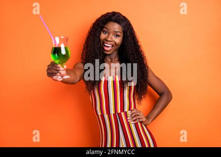 Photo of dark skin cheerful woman hold hand waist cocktail drink cheers isolated on orange color background Stock Photo