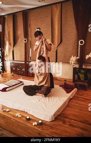 Thai yoga massage worker pulling up arms of female client Stock Photo