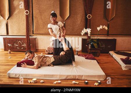 Thai massage worker pulling left leg of woman to side Stock Photo