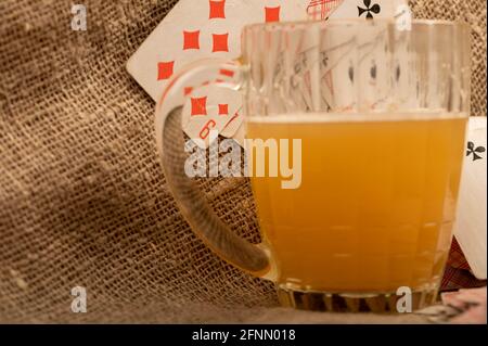 Playing cards and a mug of light unfiltered beer on a table covered with coarse cloth. Close-up, selective focus. Stock Photo