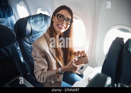 Happy lady sitting near plane window while holding box Stock Photo