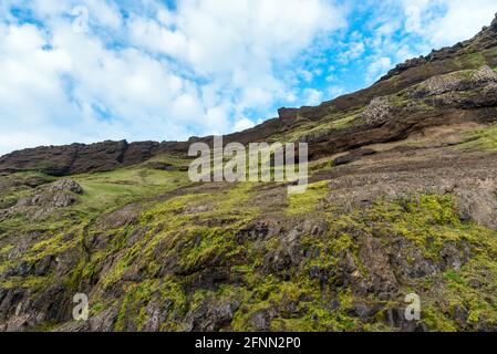 Low angle view of a steep grassy cliff under blue sky with clouds. Natural background. Stock Photo