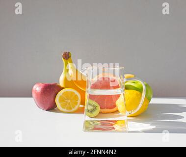 Pitcher with water and many fresh fruits on white table. Stock Photo