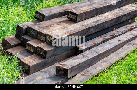 New railway sleepers impregnated with cryosote lie on green grass stacked on top of each other Stock Photo