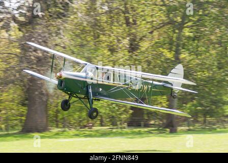 de Havilland DH87B Hornet Moth plane G-ADMT taking off from Henham Park Suffolk countryside grass airstrip. Wooded area by park runway Stock Photo