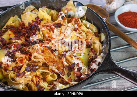 rustic hungarian pasta dish Turos csusza with cottage cheese, quark and bacon served in a cast iron pan on a table Stock Photo