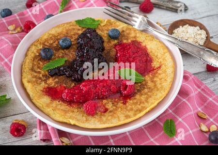 Healthy breakfast pancake made with gluten free oatmeal and served with pureed fresh berries on a plate. Stock Photo