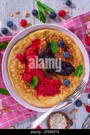 Healthy breakfast pancake made with gluten free oatmeal and served with pureed fresh berries on a plate. Stock Photo