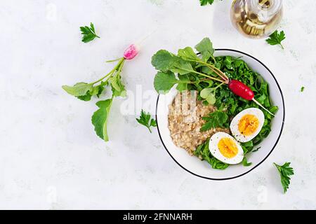 Breakfast oatmeal porridge with boiled eggs, radish and green herbs. Healthy balanced food. Top view, above Stock Photo