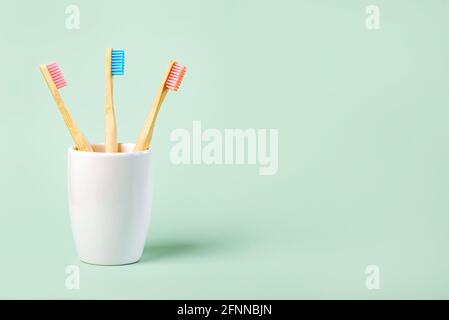 three colored bamboo toothbrushes in a ceramic glass with copy space on a green background Stock Photo