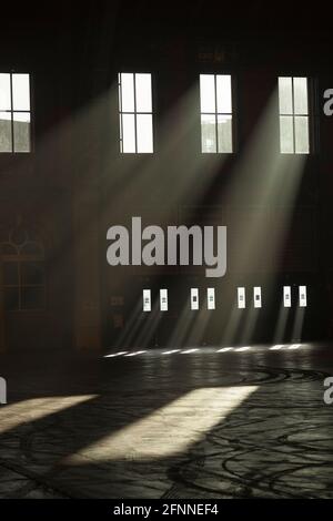 Atmospheric sunbeams streaming through the the windows of a large old building. The dusty interior atmosphere has created these striking beams Stock Photo