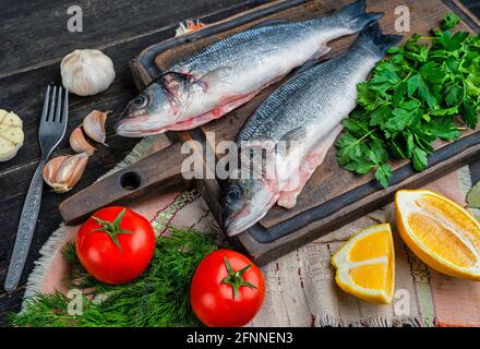 Fresh sea bass fish with herbs and lemon on a wooden cutting board. Top view Stock Photo